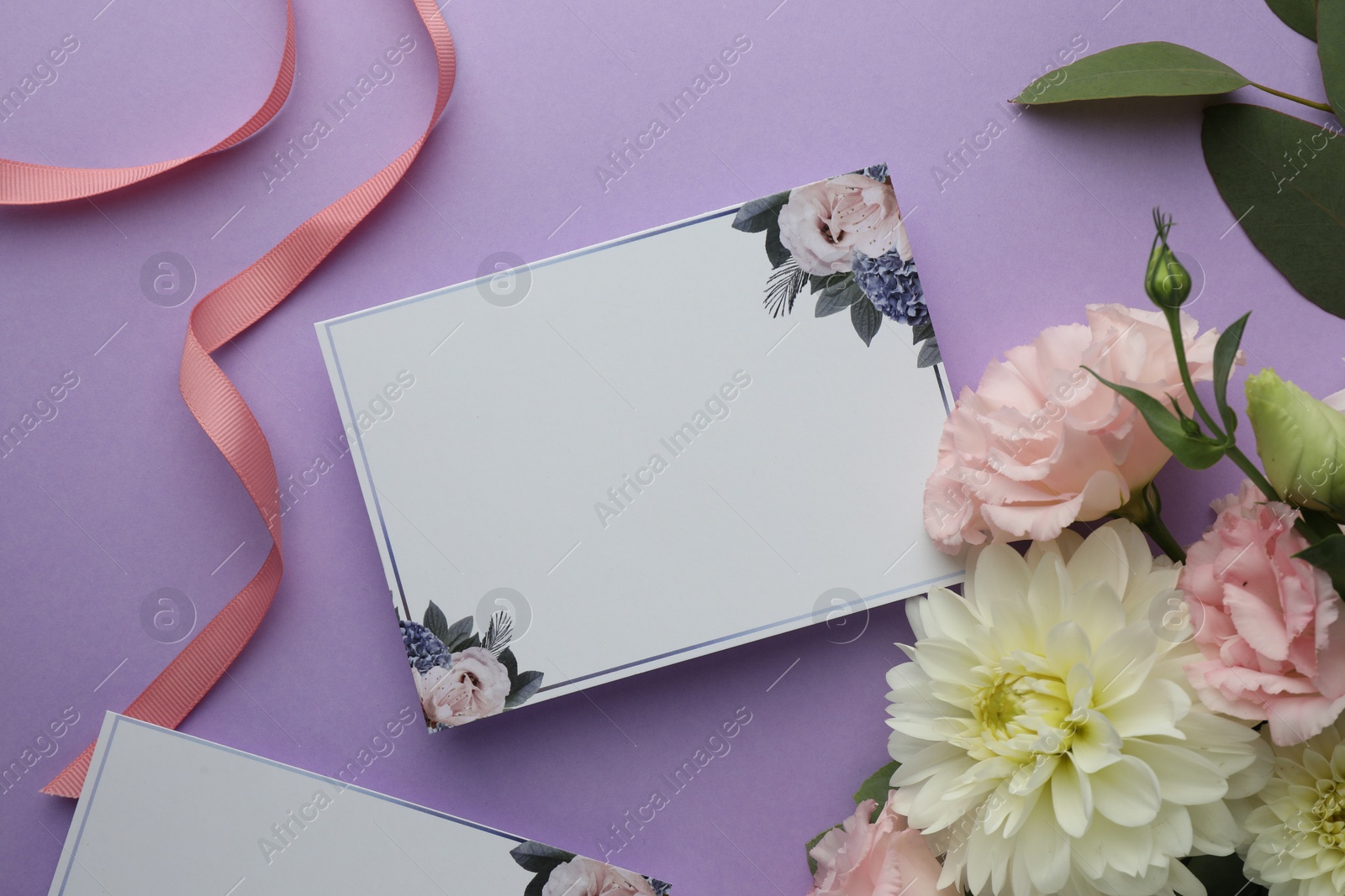 Photo of Blank invitation card and beautiful flowers on violet background, flat lay. Space for text