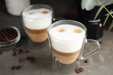 Photo of Glass cups of delicious latte macchiato and scattered coffee beans on grey table