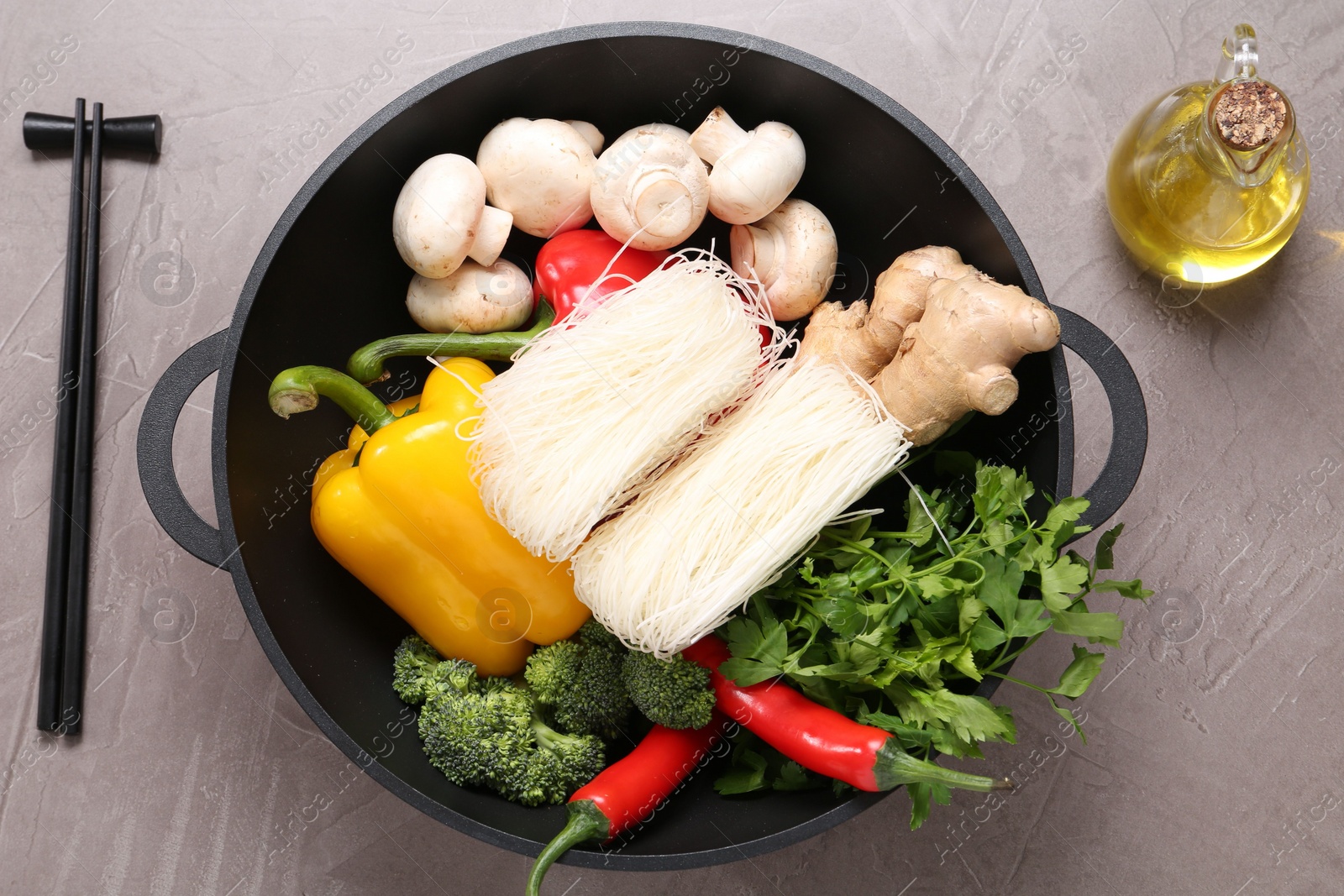 Photo of Wok, chopsticks and different products on grey textured table, flat lay