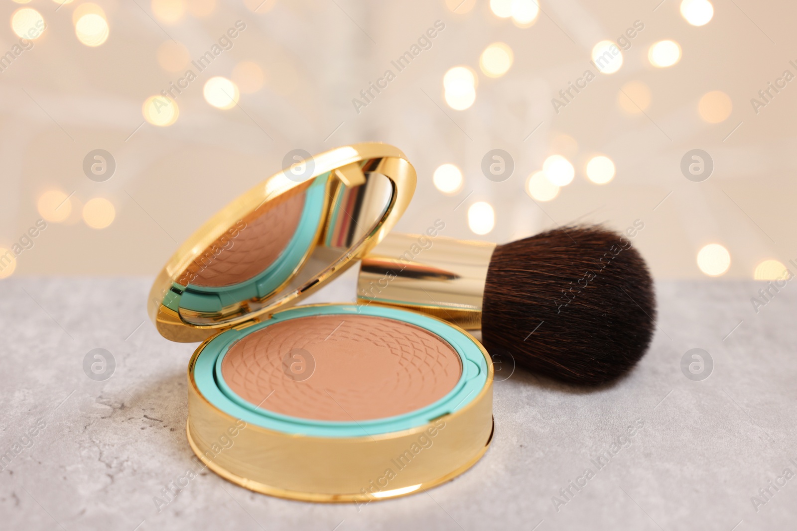 Photo of Face bronzer and makeup brush on grey textured table against blurred lights, closeup