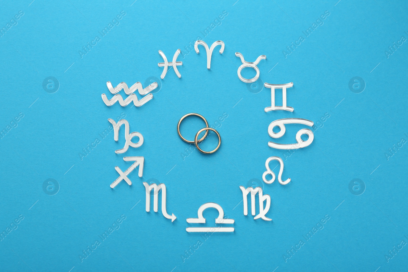 Photo of Zodiac signs and wedding rings on light blue background, flat lay