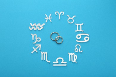 Zodiac signs and wedding rings on light blue background, flat lay