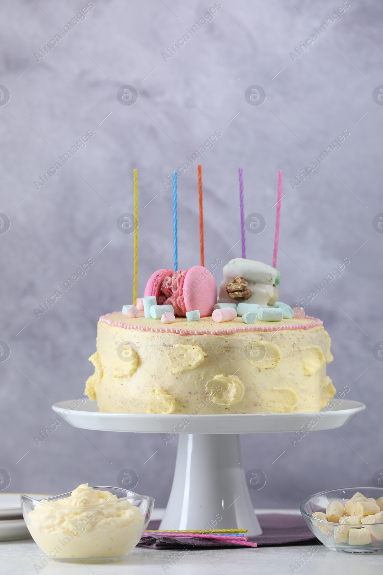 Photo of Delicious cake decorated with macarons, marshmallows and candles served on white table against grey background