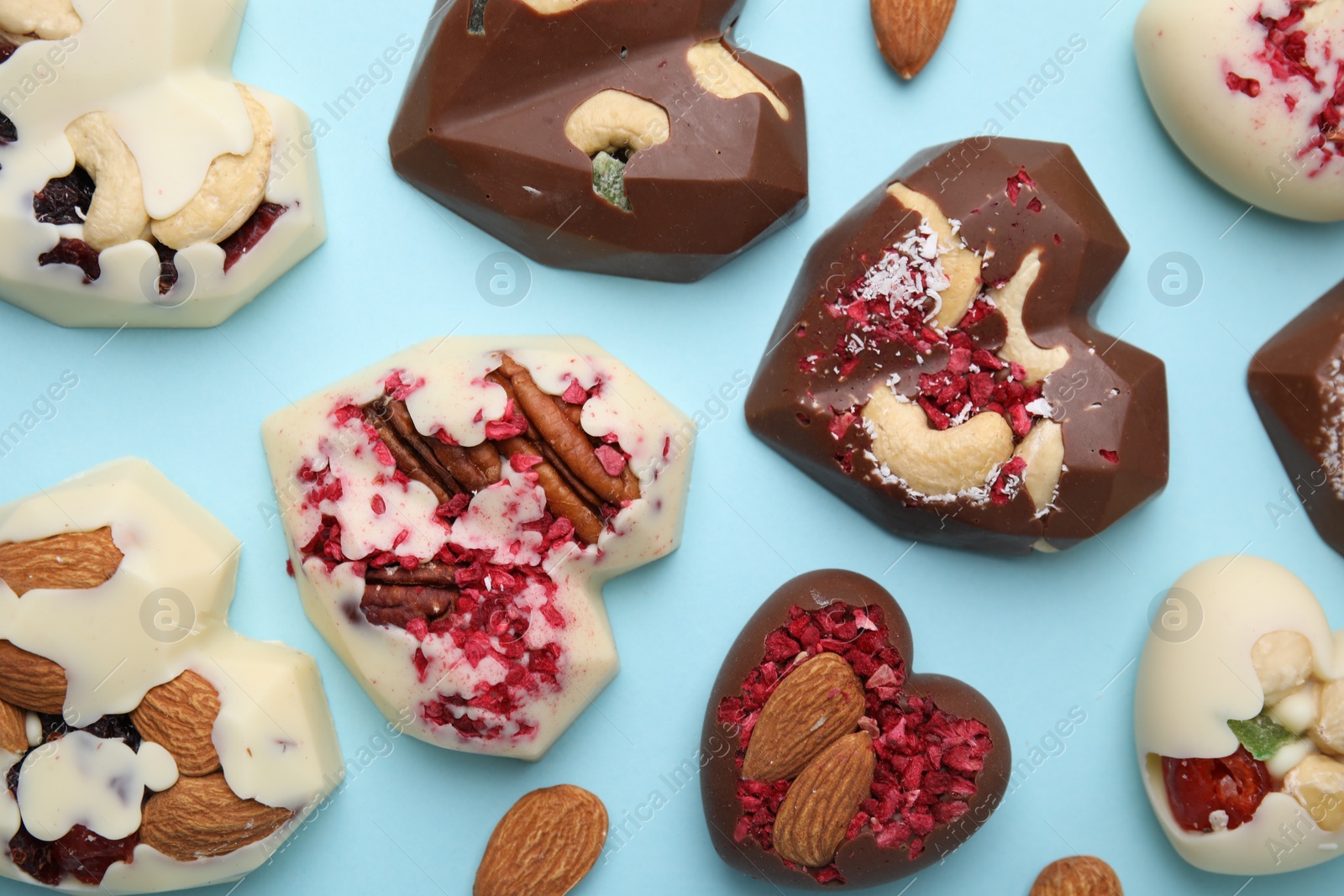 Photo of Tasty chocolate heart shaped candies with nuts on light blue background, flat lay