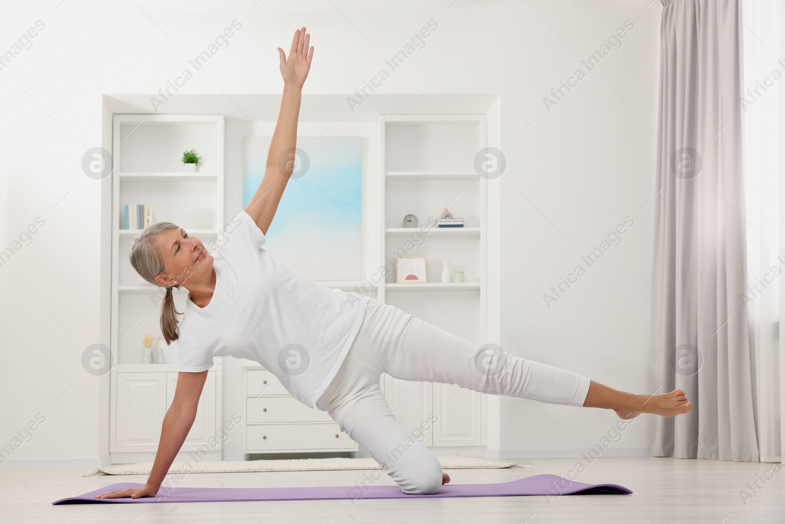 Photo of Happy senior woman practicing yoga on mat at home