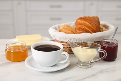 Photo of Breakfast time. Fresh croissants, coffee, jam, honey and sweetened condensed milk on white table