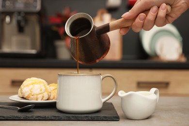 Photo of Woman pouring coffee from jezve into cup at table indoors, closeup. Turkish coffee