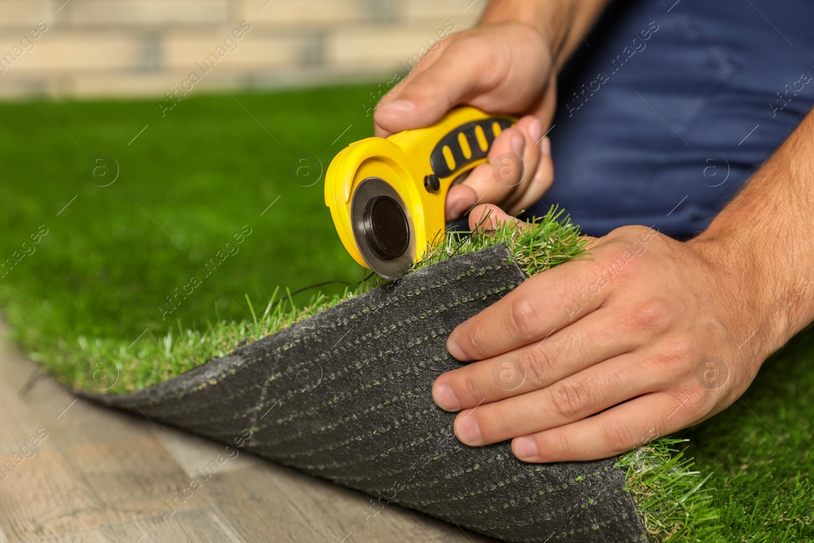 Photo of Man cutting artificial grass carpet indoors, closeup