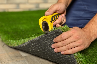 Man cutting artificial grass carpet indoors, closeup