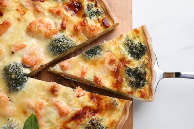 Taking piece of delicious homemade quiche with salmon and broccoli from wooden board on white table, top view