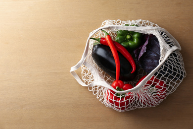 Different fresh vegetables in eco mesh bag on wooden table, top view