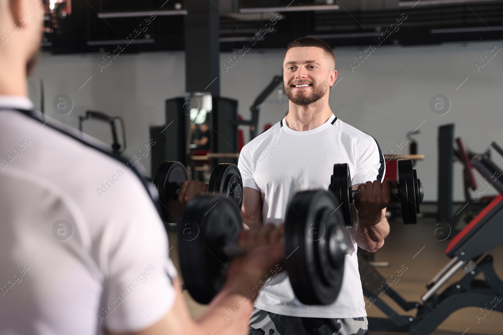 Photo of Man training with dumbbells near mirror in gym