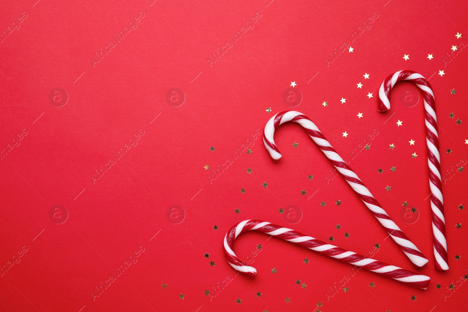 Photo of Delicious Christmas candy canes and confetti on red background, flat lay. Space for text