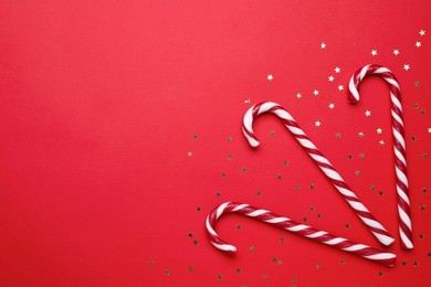 Photo of Delicious Christmas candy canes and confetti on red background, flat lay. Space for text