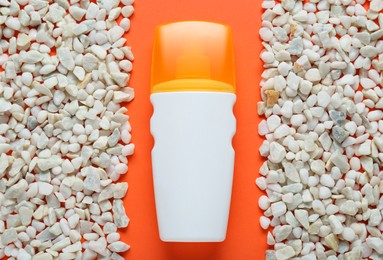 Bottle of suntan cream and white marble pebbles on orange background, flat lay