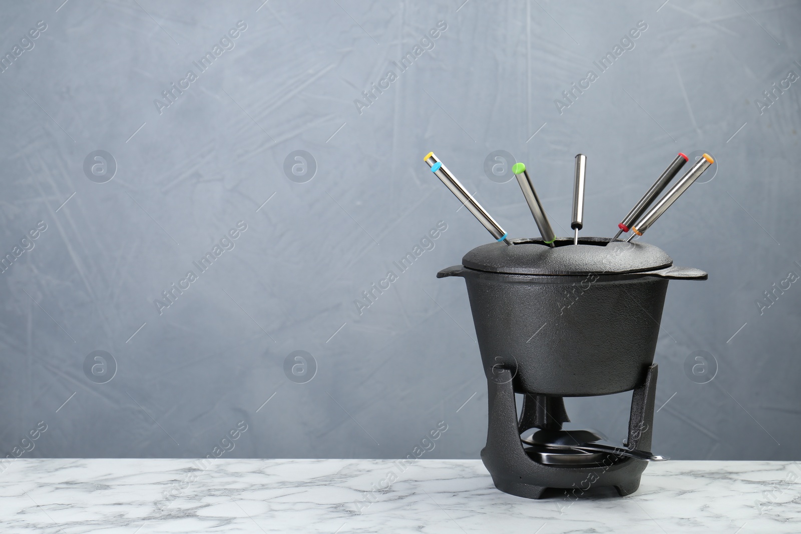 Photo of Fondue set on white marble table against light grey background, space for text