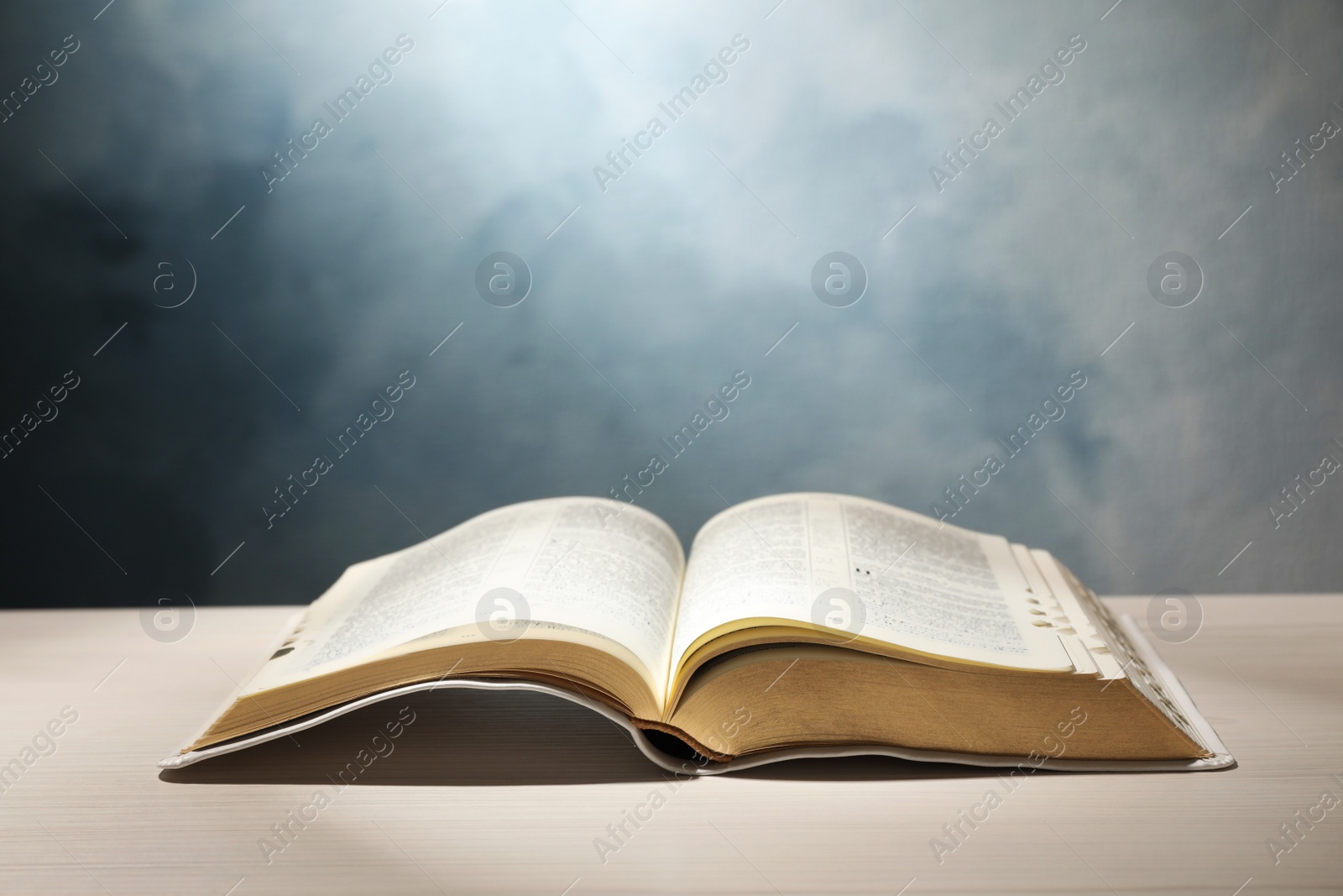 Photo of Open Bible on white wooden table against color background. Christian religious book
