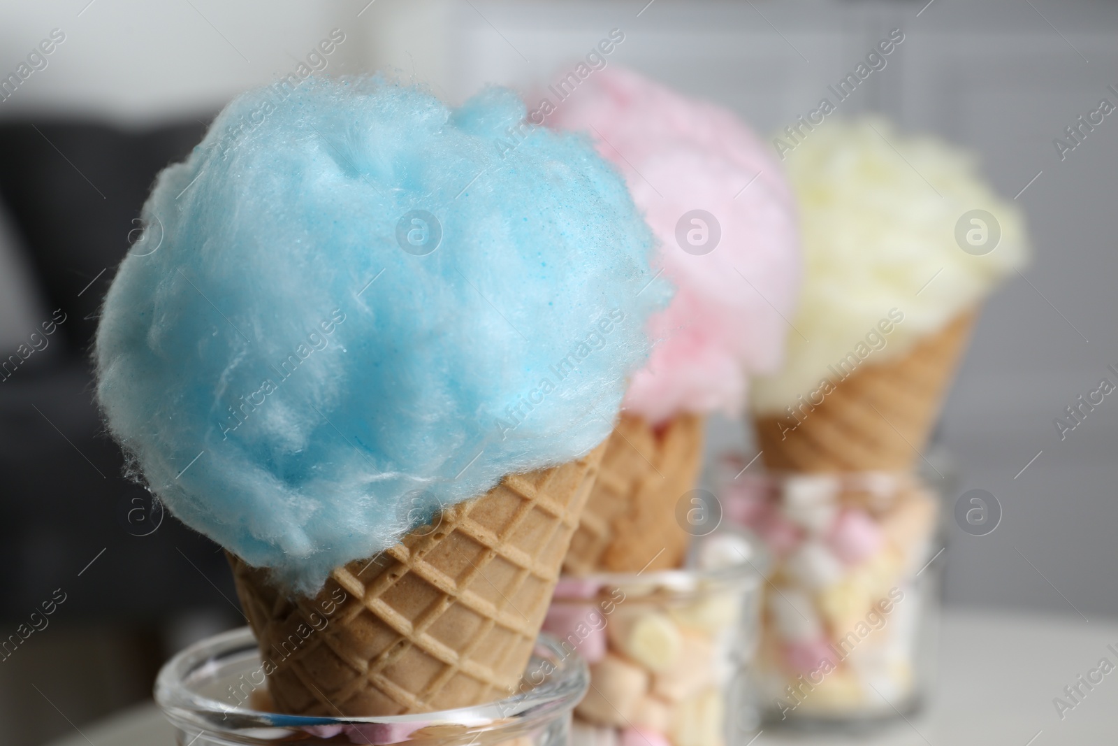 Photo of Sweet cotton candies in waffle cones on blurred background, closeup