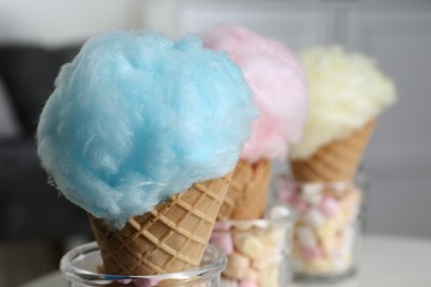 Sweet cotton candies in waffle cones on blurred background, closeup