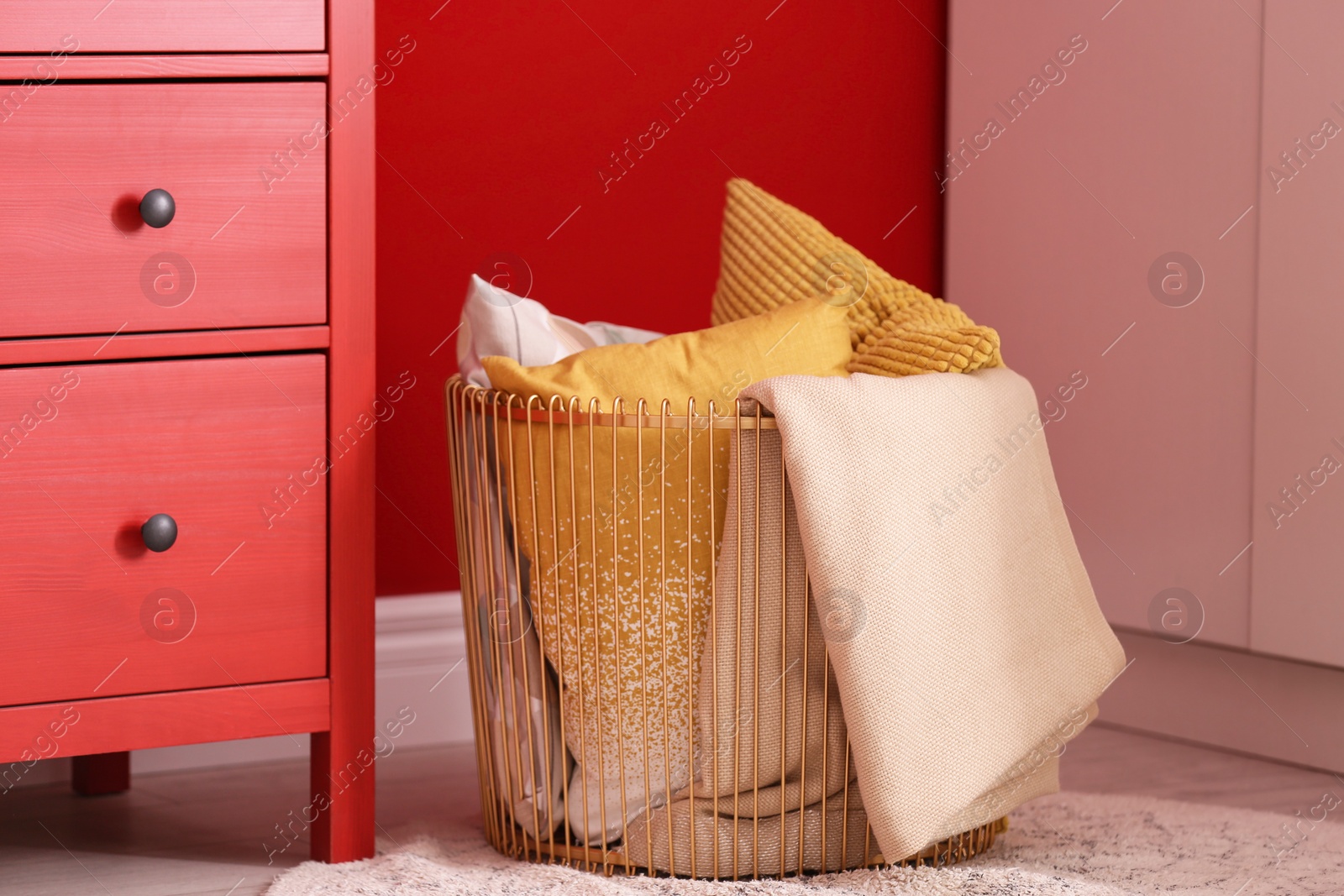 Photo of Basket with blanket and pillows near red wall indoors