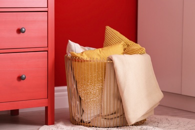 Basket with blanket and pillows near red wall indoors