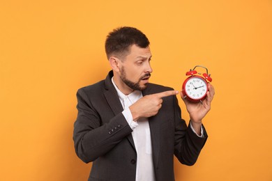 Photo of Emotional man with alarm clock on orange background. Being late concept