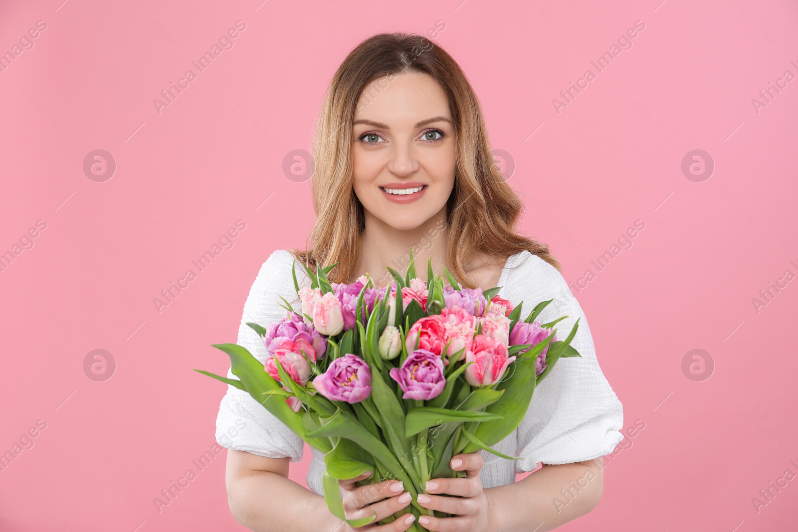 Photo of Happy young woman with bouquet of beautiful tulips on pink background