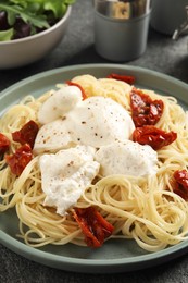 Photo of Delicious spaghetti with burrata cheese and sun dried tomatoes on grey table, closeup