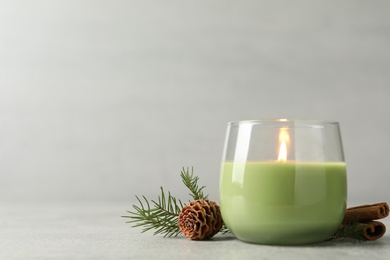 Composition with burning candle and pinecone on light grey table, space for text