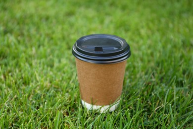 Photo of Paper cup with hot coffee on green grass outdoors, closeup. Takeaway drink