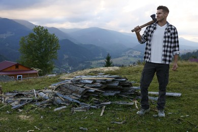 Handsome man with axe and cut firewood in mountains