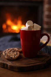 Photo of Delicious sweet cocoa with marshmallows, cookies and blurred fireplace on background