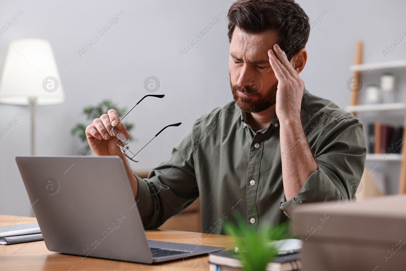 Photo of Tired man suffering from headache at workplace