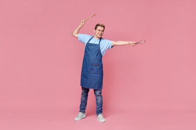Portrait of happy confectioner holding spatula and whisk on pink background, space for text