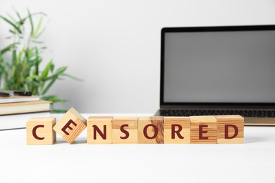 Photo of Wooden cubes with word Censored, books and laptop on white table indoors, space for text