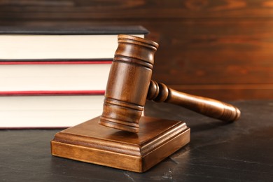 Photo of Wooden gavel and stack of books on dark textured table, closeup