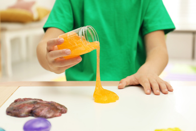 Little boy pouring slime onto table indoors, closeup