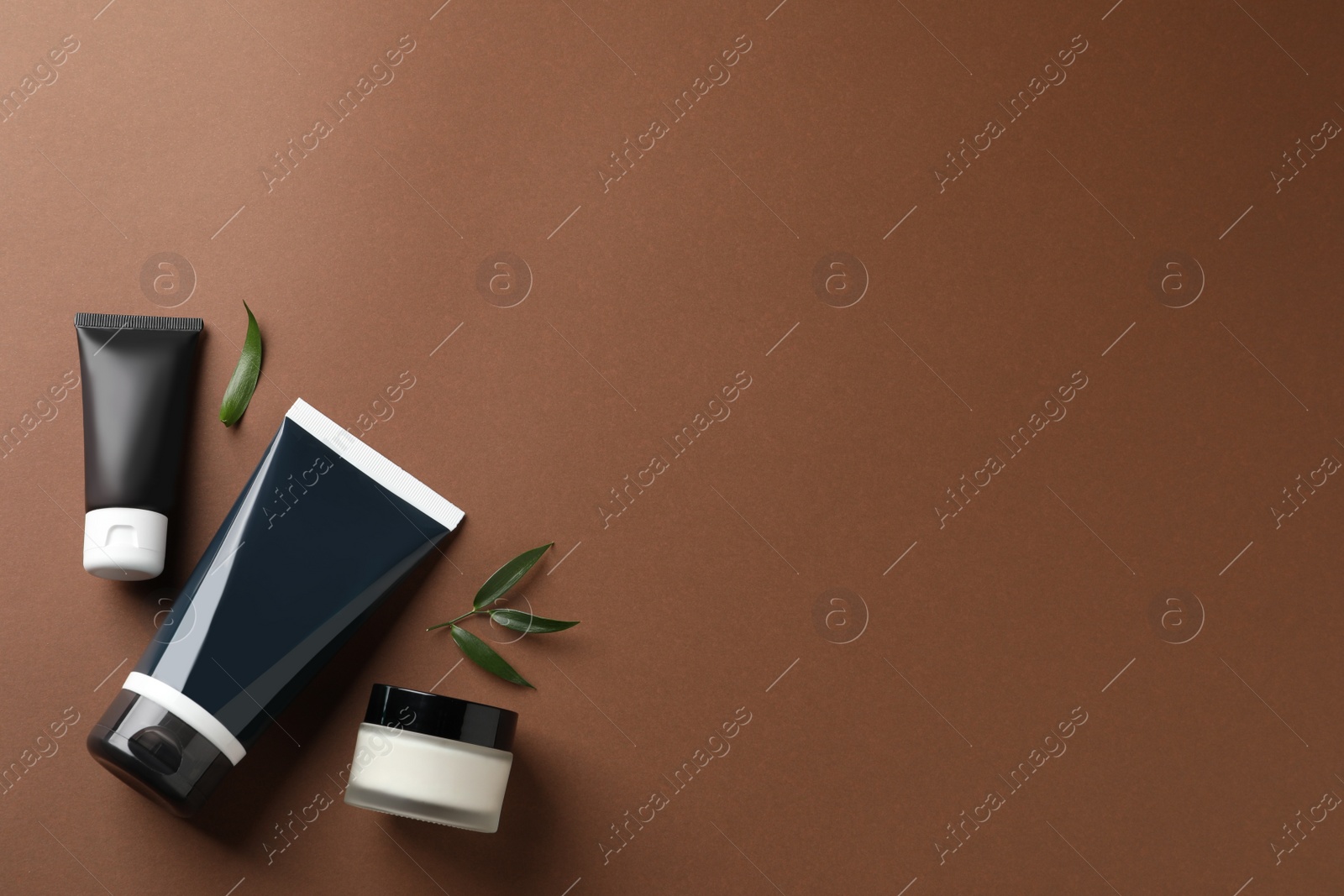 Photo of Tubes and jar of men's facial cream on brown background, flat lay. Space for text