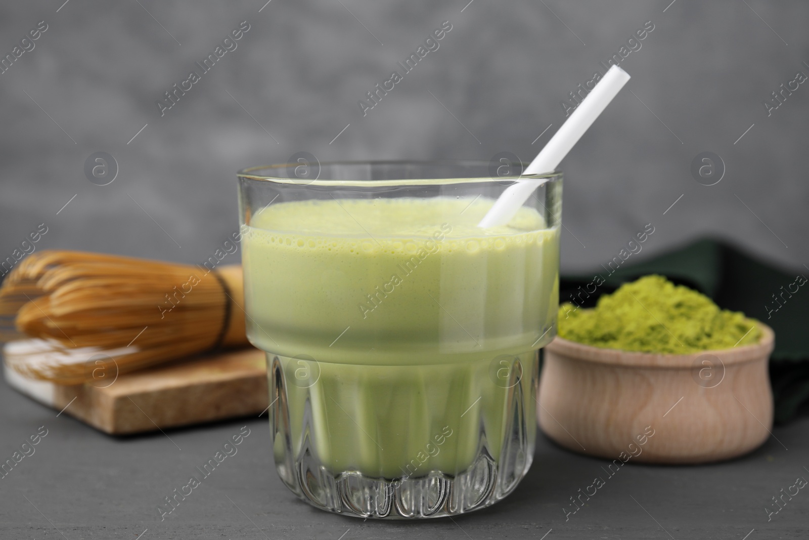 Photo of Glass of tasty matcha smoothie, powder and whisk on grey table, closeup