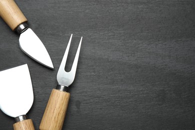 Photo of Cheese knives and fork on black background, flat lay. Space for text