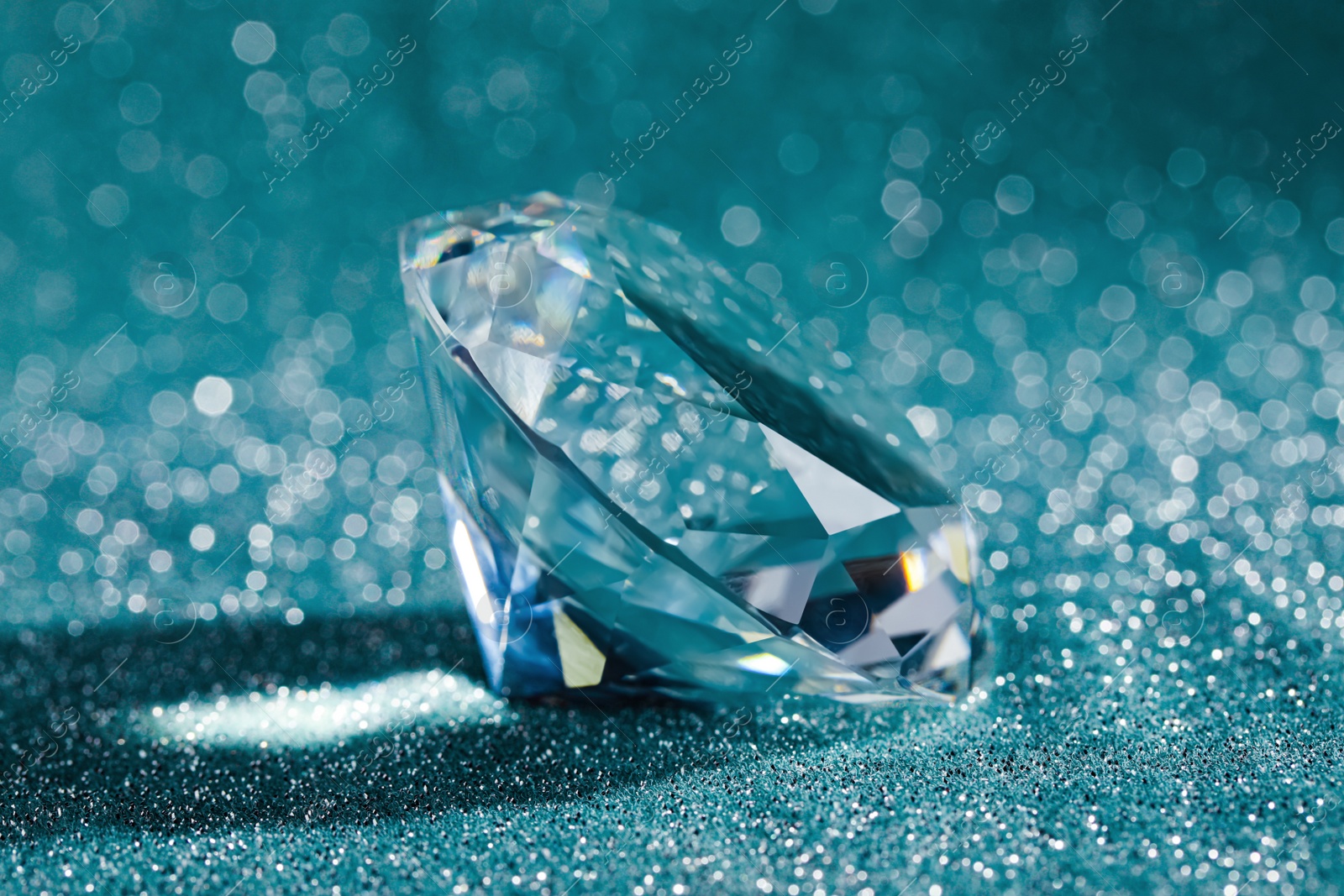 Photo of Beautiful dazzling diamond on shiny glitter background, closeup. Precious gemstone