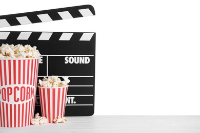 Cups with delicious popcorn and clapperboard on wooden table against white background