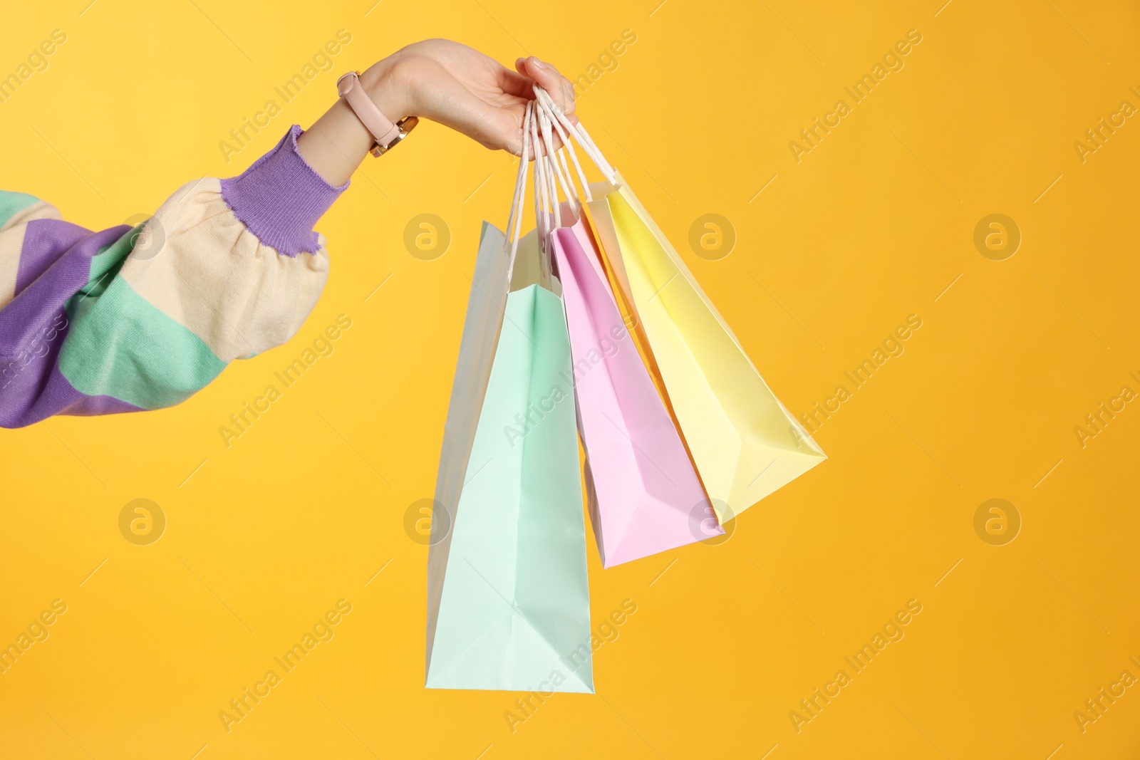 Photo of Woman holding shopping bags on yellow background, closeup. Big sale