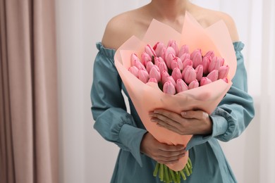 Photo of Woman holding bouquet of pink tulips indoors, closeup