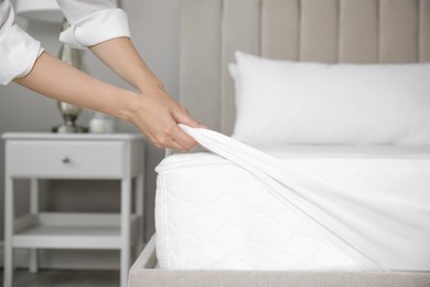 Woman putting white fitted sheet over mattress on bed indoors, closeup