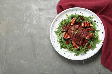 Photo of Plate of tasty bresaola salad with figs, sun-dried tomatoes and balsamic vinegar on grey table, top view. Space for text