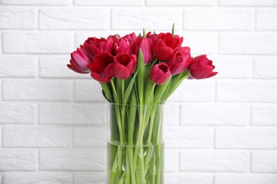Bouquet of beautiful tulips in glass vase near white brick wall
