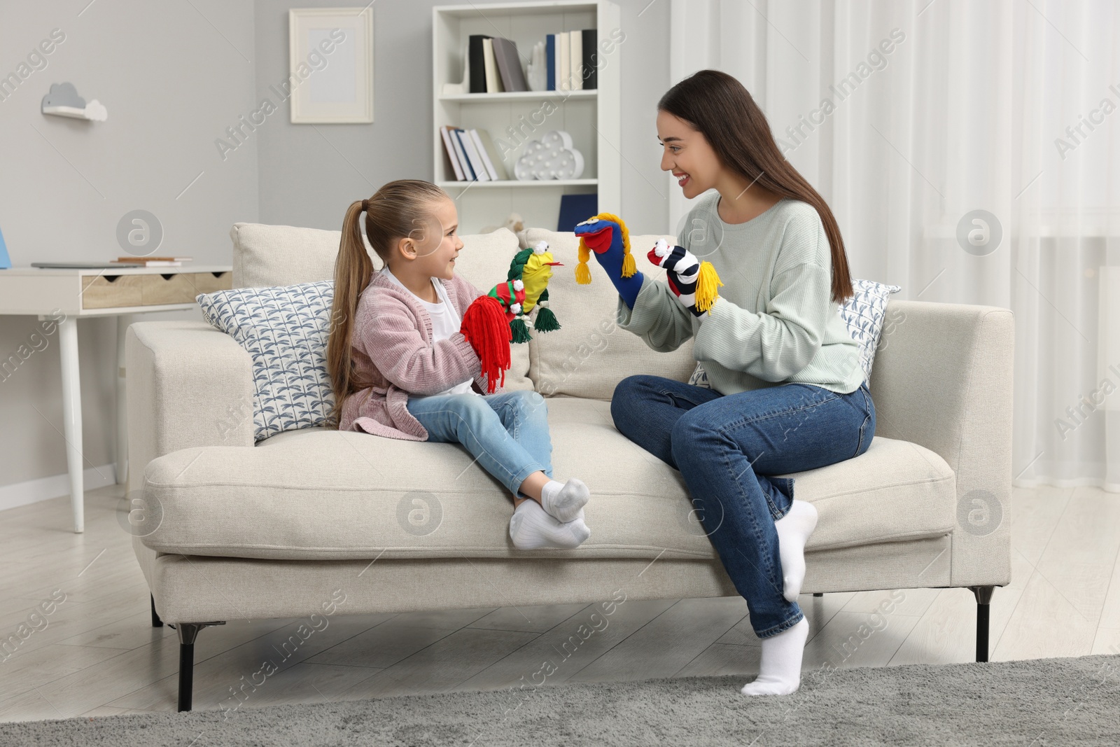 Photo of Happy mother and daughter playing with funny sock puppets together at home