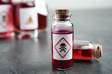Photo of Glass vials of poison with warning sign on grey stone table, closeup