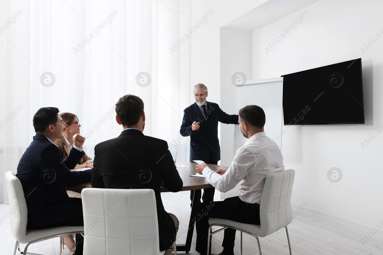 Photo of Business conference. Group of people listening to senior speaker report near tv screen in meeting room